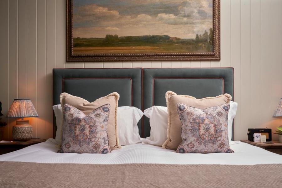 A painting of English countryside hangs above a large bed with decorative cushions